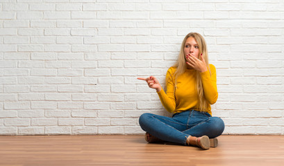 Young girl sitting on the floor pointing finger to the side with a surprised face