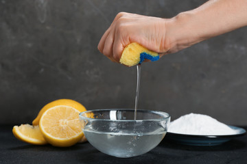 Woman squeezing out sponge over bowl with water and baking soda on dark table