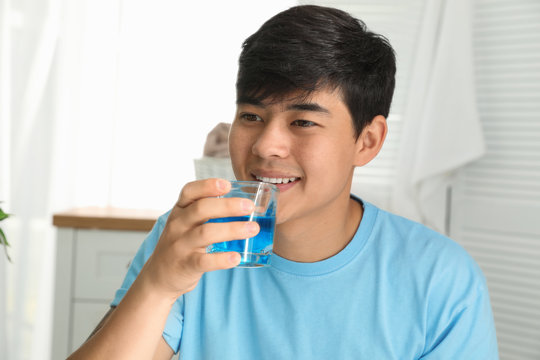 Man holding glass with mouthwash in bathroom. Teeth care