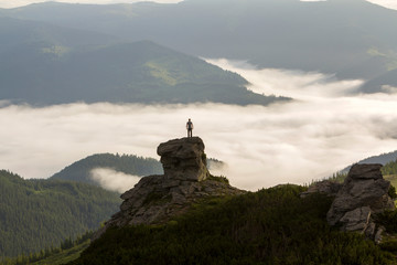 Silhouette of athletic climber tourist on high rocky formation on mountain valley filled with white...