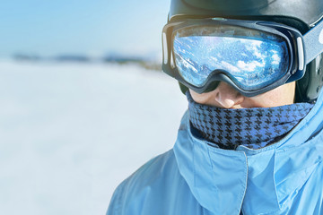 Close up of the ski goggles of a man with the reflection of snowed mountains.  A mountain range reflected in the ski mask.  Man  on the background blue sky. Wearing ski glasses. Winter Sports.