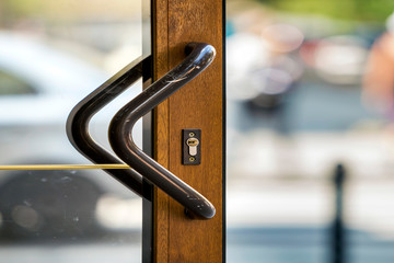 Close-up of plastic or wooden modern brown door with transparent glass surface and big metal handle on blurred bright copy space bokeh background. Entrance, exit, office or hallway.