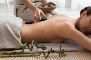 Beautiful young woman getting hot stone massage in spa salon