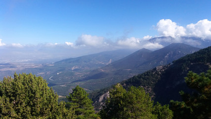 Obraz premium Natural scenery at Denizli Kent Forest on a bright sunny morning, with green trees, mountaintops, bright blue skies and fluffy white clouds overlooking a green valley.