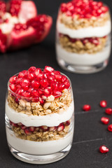 Pomegranate parfait - sweet organic layered dessert with granola flakes, yogurt and fruit seeds on black background.