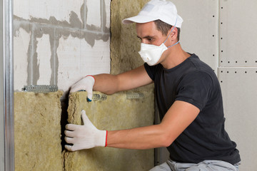 Worker in protective respirator mask insulating rock wool insulation in wooden frame for future...