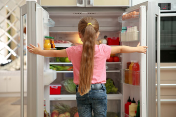 Cute little girl choosing food in refrigerator at home