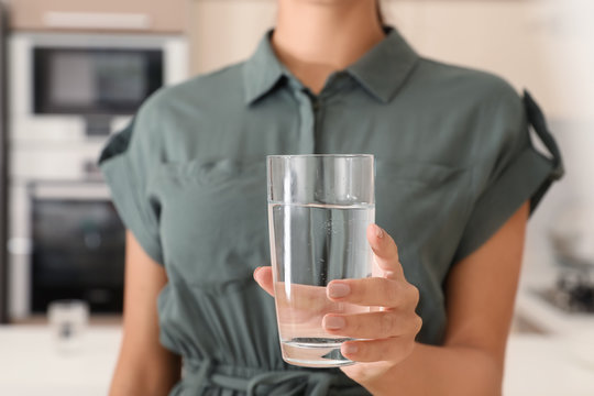 Woman holding glass with pure water in kitchen, closeup
