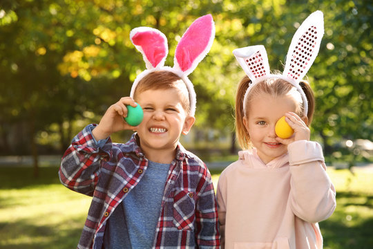 Cute little children with bunny ears holding Easter eggs in park