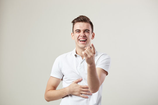 Guy dressed in a white t-shirt and jeans laughs and keeps hand on the belly on a white background in the studio