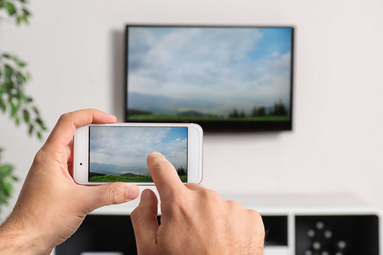 Woman With Smartphone Connected To TV Set In Living Room