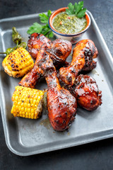 Traditional barbecue chicken drumsticks with corn and chimichurri sauce as top view in a silber fryer © HLPhoto