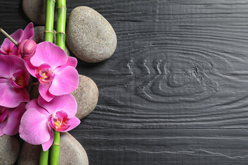 Spa stones with orchid flowers and bamboo on dark wooden background, top view. Space for text