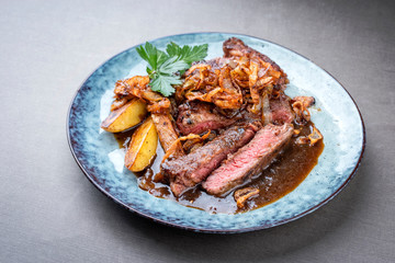 Traditional dry aged sliced roast beef with fried onion rings and potato chips as closeup on a plate with brown sauce with copy space