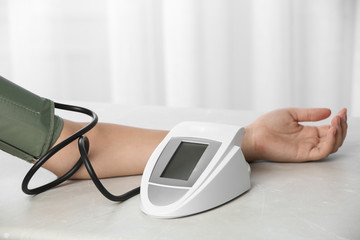 Woman checking pulse and blood pressure with sphygmomanometer on table, closeup