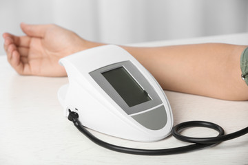 Woman checking pulse and blood pressure with sphygmomanometer on table, closeup