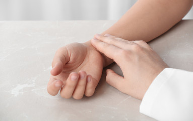 Doctor checking patient's pulse on table, closeup