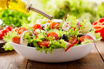 Cooking salad. olive oil pouring into bowl of fresh salad