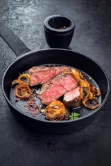 Fototapeten Modern Style classic dry aged sliced roast beef with fried onion rings served as closeup in a minimalistic design cast-iron skillet © HLPhoto