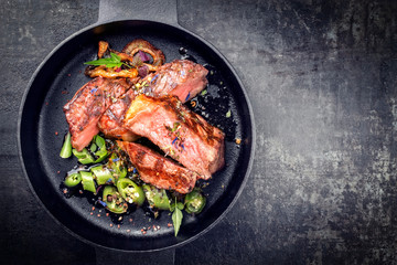 Modern Style classic dry aged sliced roast beef with fried onion rings and chili served as top view in a minimalistic design cast-iron skillet with copy space right © HLPhoto