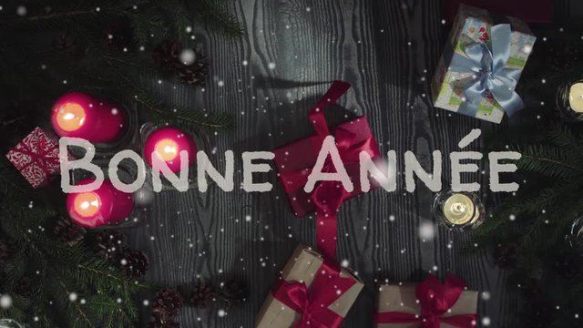 Animation Bonne Annee - Happy New Year in french, white letters, red candles and gift, falling snow. Top view