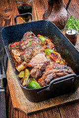 Traditionell gegrillte Lammhaxen mit Zitrone und  Tomaten als closeup in einer alten Bratpfanne