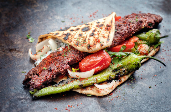 Traditional Adana kebap on a skewer with tomato and yogurt as closeup on a flatbread