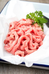 Raw veal strips for traditional Swiss zürcher geschnetzeltes with herbs as closeup in a white skillet