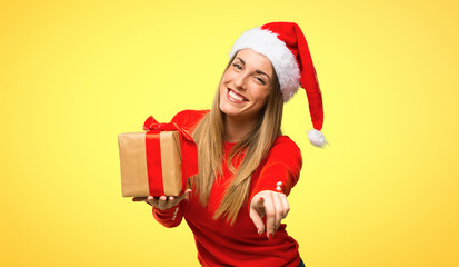 Blonde woman dressed up for christmas holidays points finger at you while smiling on yellow background