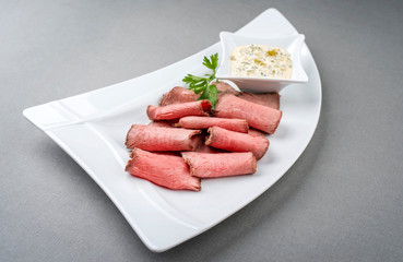 Traditional lunch meat with sliced cold cuts roast beef and remoulade as closeup on a white plate with copy space