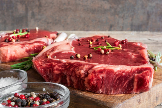 Raw beef steaks with spices and rosemary on wooden board over rustic wooden background