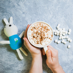 female hands hold big mug with cacao and marshmallow on gray background.
