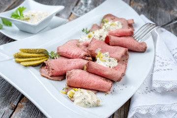 Traditional lunch meat with sliced cold cuts roast beef and remoulade as closeup on a white plate on a wooden table