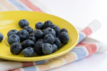 Blueberries (heath berry) in a yellow plate on coloful linen kitchen towel