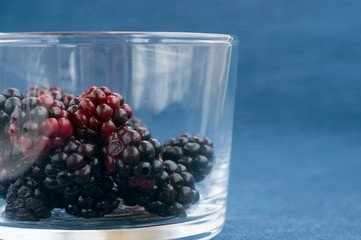 Fresh raw blackberries in a glass on blue background