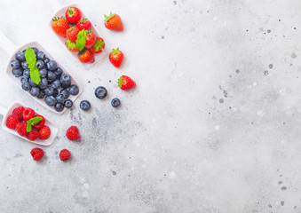 Fresh raw organic berries in white scoop spoon on kitchen table background. Space for text. Top view. Strawberry, Raspberry, Blueberry and Mint leaf