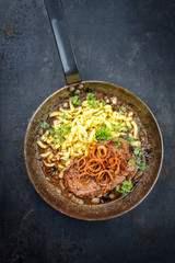 Traditioneller Zwiebelrostbraten aufgeschnitten mit schwäbischen Spätzle und Röstzwiebel als Draufsicht in einer schmiedeeisernen Pfanne mit brauner Sauce 