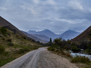 dirt road leading to high mountains passing along a mountain river