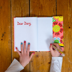Young girl writing the words dear diary in a vintage book