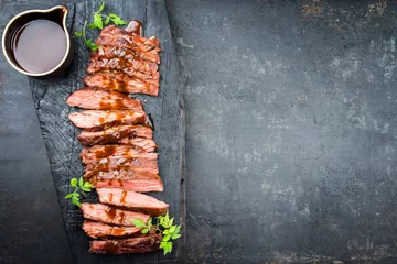 Poster Im Rahmen Traditional American barbecue dry aged flank steak sliced with hot sauce and chili as top view on an old carbonized board with copy space right © HLPhoto
