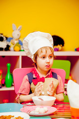 Sweet little cute child girl is learning how to make a cake in the home kitchen.