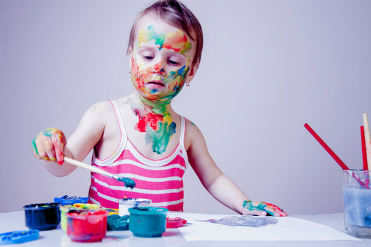 Art, creativity, beauty childhood concept. Portrait of little cute child girl painting with colorful hands and face.