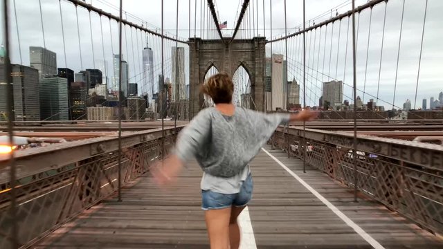 Happy young woman walking and dancing in Brooklyn Bridge at day time