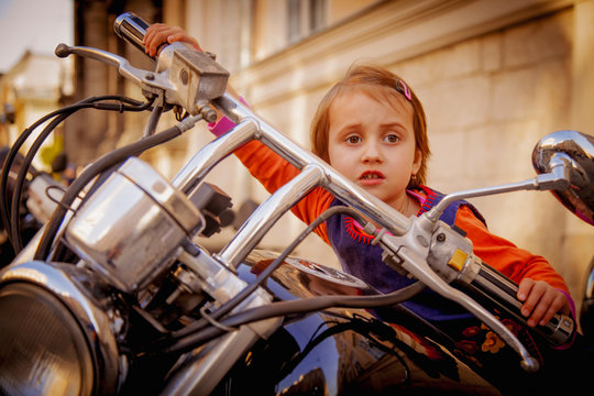 Beautiful little biker child girl on a motorcycle as a symbol of freedom, adventure and travel. Humorous photography.