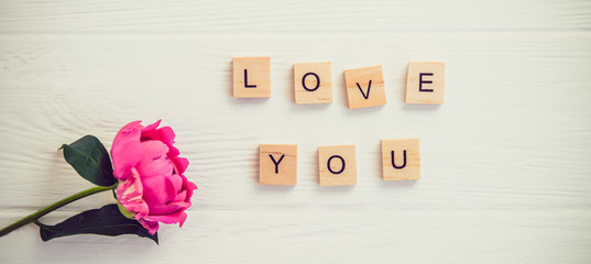 Top view Message I love you spelled in wooden blocks with pink peony flower on white wooden table....