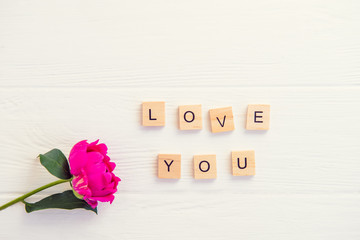 Top view Message I love you spelled in wooden blocks with purple pink peony flower on white wooden...