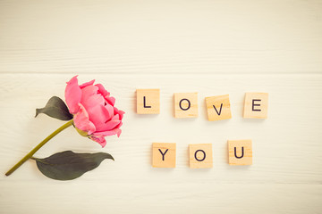 Top view Message I love you spelled in wooden blocks with pink peony flower on white wooden table. Love, Valentines day background. Gift, greeting, compliment concept. Vintage tonning. Copy space.