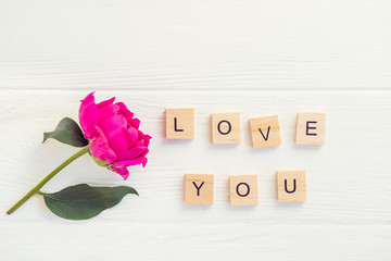 Top view Message I love you spelled in wooden blocks with purple pink peony flower on white wooden...