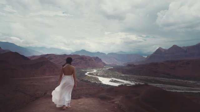 Hispanic bride in a long white wedding dress walking on the big rocks on the top of the mountains, Bride alone with nature on a windy day. Slow motion.