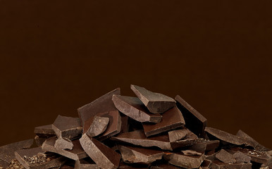 Broken or cracked dark chocolate parts pile or heap on brown background